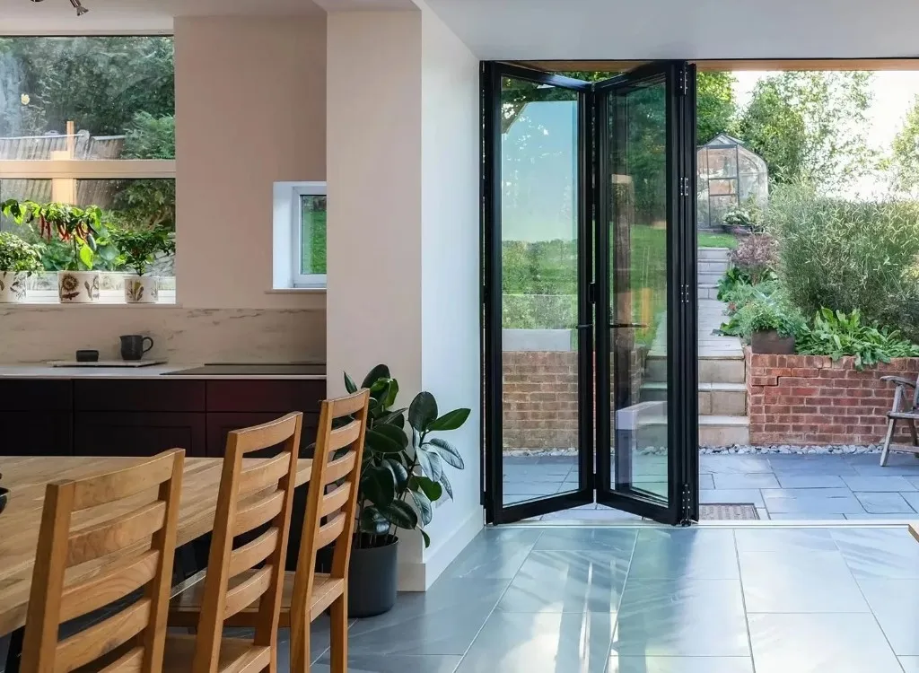 Black bi-fold doors folded open from a kitchen to a garden